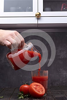 Fresh tomato juice in a glass with tomatoes, with parsley on a dark background.