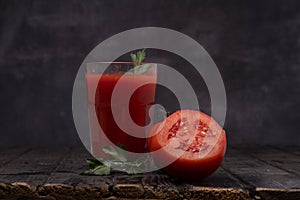 Fresh tomato juice in a glass with tomatoes, with parsley on a dark background.