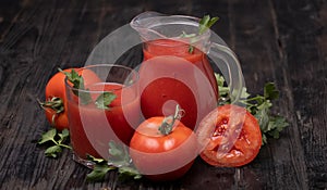 Fresh tomato juice in a glass with tomatoes, with parsley on a dark background.