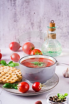 Fresh tomato soup with basil in a bowl and fresh vegetables on the table. Vertical view