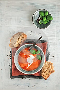 Fresh Tomato soup in a bowl with tomatoes and basil on a white kitchen table