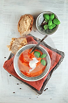 Fresh Tomato soup in a bowl with tomatoes and basil on a white kitchen table