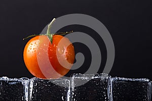 Fresh tomato on wet ice cubes on black background. Selective foc