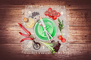 Fresh tomatoes, chili pepper and other spices and herbs around modern Turquoise plate in the center of wooden table and cloth