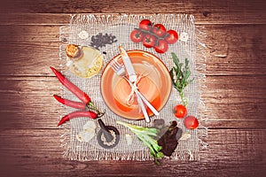 Fresh tomatoes, chili pepper and other spices and herbs around modern Turquoise plate in the center of wooden table and cloth