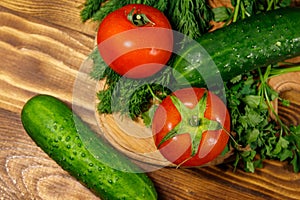 Fresh tomatoes, cucumbers, parsley and dill on cutting board on wooden table