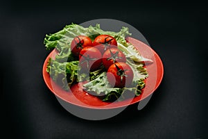 Fresh tomatoes with drops of water and lettuce on a red plate on a dark background
