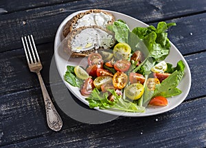 Fresh tomatoes and garden herbs salad and cheese sandwich on a white ceramic plate on dark wooden background.