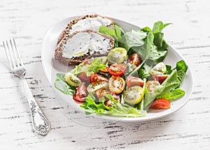 Fresh tomatoes and garden herbs salad and cheese sandwich on a white ceramic plate on a light wooden background.