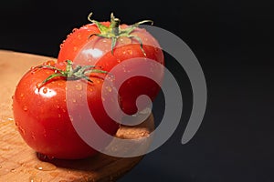 Fresh tomatoes with water drops on a black background close-up.