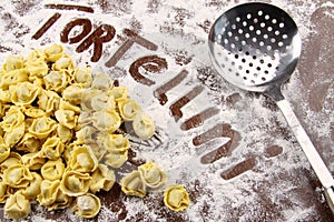 Fresh tortellini and utensil with flour on table