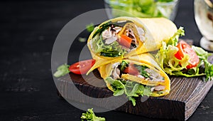 Fresh tortilla wraps with chicken and fresh vegetables on wooden board.