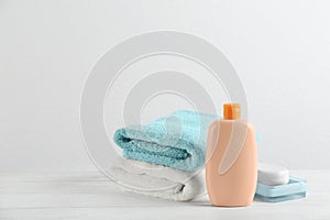 Fresh towels and bottle of cosmetic product on white wooden table