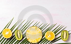 Fresh tropic fruits green kiwi, pineapples,oranges on palm tree leaf on pink background. Top view, flat lay