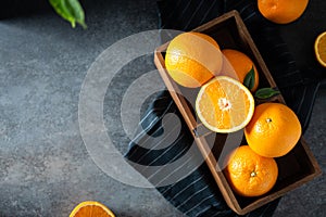 Fresh tropical fruits in a wooden delivery box on dark stone background. Sweet juicy oranges in wooden basket, top view flat lay