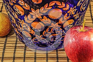 Fresh tropical and subtropical fruits in a large blue crystal vase. Wicker bamboo stand on the dining table. Close up macro