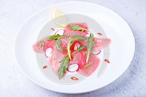 Fresh tuna carpaccio with arugula, radish, chili and lemon. Traditional cold appetizer of Italian cuisine. Close-up.
