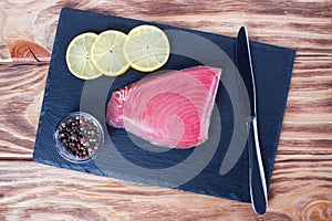 Fresh tuna fillet on the stone plate. Fish steak on a cutting board with lemon slices and allspice. Red fish textured