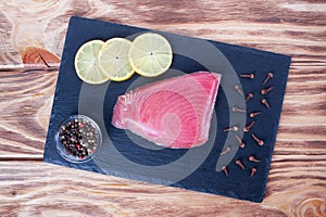 Fresh tuna fillet on the stone plate. Fish steak on a cutting board with lemon slices, clove seeds and allspice. Red