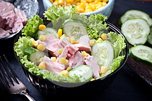 Fresh tuna salad with corn and lettuce leaves, sauce and fresh cucumbers, closeup