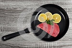 Fresh tuna steak with slices of lemons in skillet.