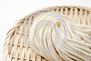 Fresh udon noodles in a bamboo colander placed on a white background