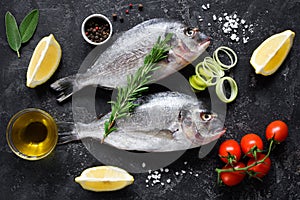 Fresh uncooked dorado or sea bream fish with lemon slices, spices, herbs and vegetables. Mediterranean food. Top view