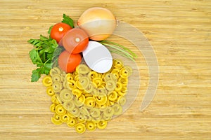 Fresh uncooked gold colored pasta, tomatoes, egg, parsley and onion