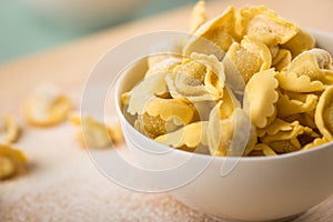 Fresh, uncooked Italian Cappelletti Tortellini pasta with flour and semolina  in porcelain bowl and on wooden board and pastel