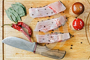 Fresh uncooked pieces of silver carp fish with red chile pepper, bay leaf, spices and knife on wooden board, top view.