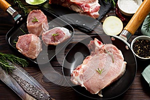 Fresh various meat. Raw pork steak and cutlets on a cast iron frying pan, spices and fresh rosemary on a kitchen wooden table