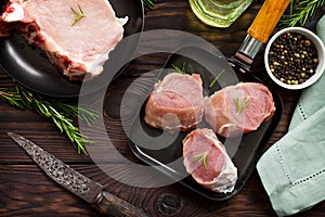 Fresh various meat. Raw pork steak and cutlets on a cast iron frying pan, spices and fresh rosemary on a kitchen wooden table.