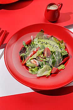 Fresh vegan green salad with avocado, tomatoes , red bell peper and nut sauce in red color boul at red and white background with