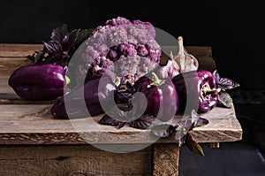 Dark purple peppers, cauliflower with leaves of basil and garlic on old rustic wooden table on black background