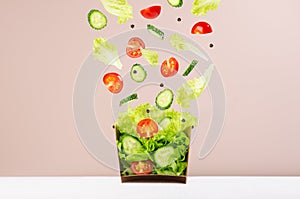 Fresh vegetable salad in craft box for take away food with falling slices of ingredients - cherry tomato, cucumber, green salad.