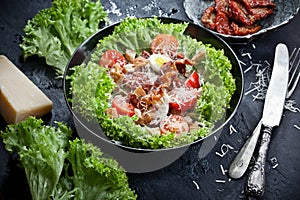 Fresh vegetable salad with green lettuce, dried tomatoes, parmesan cheese, meat, eggs and croutons on kitchen table, closeup