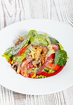 Fresh vegetable salad with lettuce, spinach, grilled mushrooms, tomatoes, sweet peppers and sesame seeds on plate