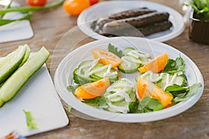 Fresh vegetable salad, on the table on the background of grilled sausages