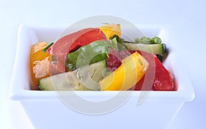 Fresh vegetable salad with tomato, cucumber, bell pepper and lettuce leaf in white bowl.