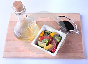 Fresh vegetable salad with tomato, cucumber, bell pepper, lettuce leaf in white bowl, olive oil and balsamic souce in