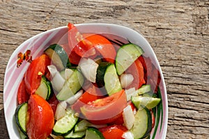 Fresh vegetable salad  with tomatoes, cucumbers, onion and olive oil on wooden table. Top view