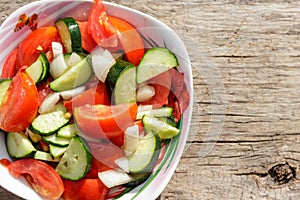 Fresh vegetable salad  with tomatoes, cucumbers, onion and olive oil on wooden table. Top view