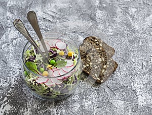 Fresh vegetable salad with white and red cabbage, cucumber, radish and cilantro in a glass jar on a stone texture.