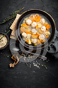 Fresh vegetable soup with meatballs and pearl barley in bowl on black background