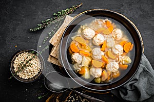 Fresh vegetable soup with meatballs and pearl barley in bowl on black background