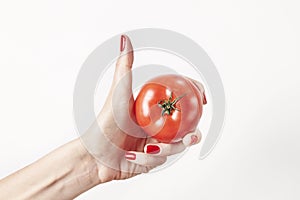 Fresh vegetable tomato in woman hand, fingers with red nails manicure, isolated on white background, healthy lifestyle concept.