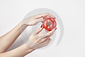Fresh vegetable tomato in woman`s hands, fingers with red nails manicure, isolated on white background, healthy lifestyle concept.