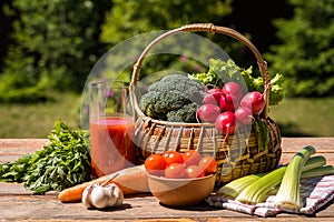 Fresh vegetables in a basket and tomato juice over green nature background