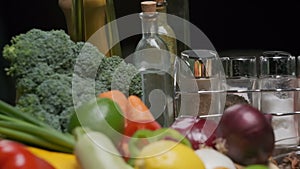 Fresh vegetables, bottles with oil and vinegar, spice jars on the kitchen table