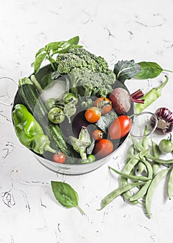 Fresh vegetables - broccoli, zucchini, beets, peppers, tomatoes, green beans, garlic, basil in a metal basket on a light